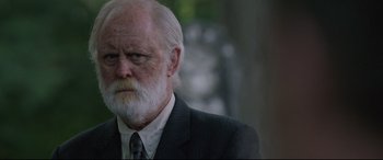 Movie still from “Pet Sematary” (2019), directed by Kevin Kölsch – An older man with a beard and a suit and tie; Close Up shot, Over the shoulder angle