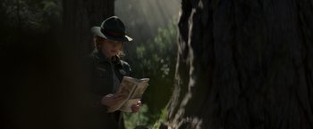 Movie still from “Pete's Dragon” (2016), directed by David Lowery – A woman reading a newspaper in a forest; Medium shot, Over the shoulder angle
