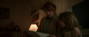 Movie still from “Pete's Dragon” (2016), directed by David Lowery – A woman and a child looking at a piece of paper in a dimly - lit room; Medium shot, Over the shoulder angle