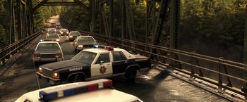 Movie still from “Pete's Dragon” (2016), directed by David Lowery – A police car driving down a road next to a bridge; Extreme Wide shot, High angle