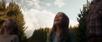 Movie still from “Pete's Dragon” (2016), directed by David Lowery – A young girl is smiling and looking up at the sky; Medium shot, Low angle