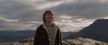 Movie still from “Pete's Dragon” (2016), directed by David Lowery – A young boy wearing a plaid coat and a necklace; Medium shot, Low angle