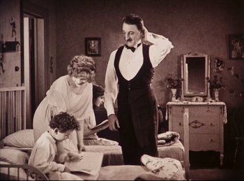 Movie still from “Peter Pan” (1924), directed by Herbert Brenon – An old photo of a man and a woman and two children; Medium shot, Low angle