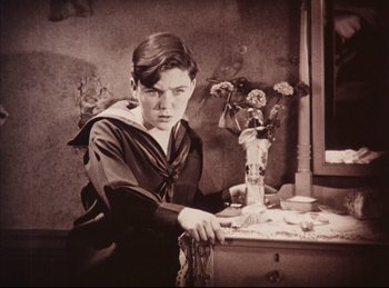 Movie still from “Peter Pan” (1924), directed by Herbert Brenon – A young man sitting at a table with a vase of flowers in front of him; Medium shot, High angle