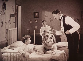 Movie still from “Peter Pan” (1924), directed by Herbert Brenon – An old black and white photo of a man and two boys and a dog in a room; Wide shot, Low angle