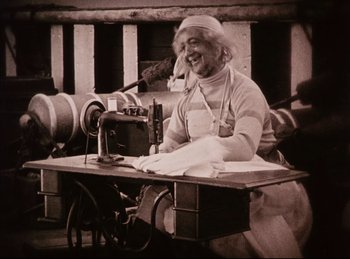 Movie still from “Peter Pan” (1924), directed by Herbert Brenon – An older woman sitting at a sewing machine; Medium shot, Low angle