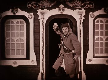 Movie still from “Peter Pan” (1924), directed by Herbert Brenon – An old photo of a man standing in front of a building; Wide shot, Low angle