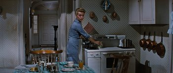 Movie still from “Peyton Place” (1957), directed by Mark Robson – A woman standing in front of an oven cooking food; Medium shot, High angle