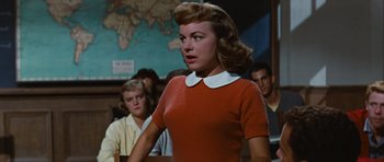 Movie still from “Peyton Place” (1957), directed by Mark Robson – A woman in a red sweater standing in front of a group of people; Medium shot, Over the shoulder angle