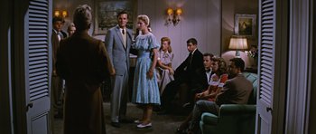Movie still from “Peyton Place” (1957), directed by Mark Robson – A man and woman standing in front of other people; Wide shot, Over the shoulder angle