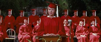 Movie still from “Peyton Place” (1957), directed by Mark Robson – A woman wearing a red graduation cap and gown standing in front of a crowd; Medium shot, Low angle