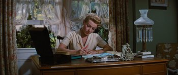 Movie still from “Peyton Place” (1957), directed by Mark Robson – A woman sitting at a desk writing on a piece of paper; Medium shot, Low angle