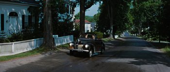 Movie still from “Peyton Place” (1957), directed by Mark Robson – An old car driving down a street next to trees; Extreme Wide shot, High angle