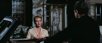 Movie still from “Peyton Place” (1957), directed by Mark Robson – A woman sitting at a table in front of a building; Medium shot, Low angle