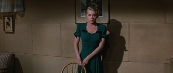 Movie still from “Peyton Place” (1957), directed by Mark Robson – A woman in a green dress standing next to a chair; Medium shot, Low angle