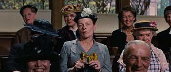 Movie still from “Peyton Place” (1957), directed by Mark Robson – An older woman holding a bow tie in front of a group of other women; Medium shot, Low angle