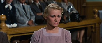 Movie still from “Peyton Place” (1957), directed by Mark Robson – A woman in a purple dress sitting in front of a group of people; Close Up shot, Low angle