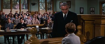 Movie still from “Peyton Place” (1957), directed by Mark Robson – A man standing in front of a crowd in a courtroom; Medium shot, Low angle