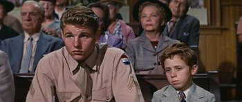 Movie still from “Peyton Place” (1957), directed by Mark Robson – A group of people sitting in front of each other in a room; Medium shot, Over the shoulder angle