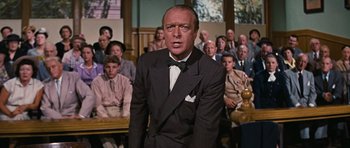 Movie still from “Peyton Place” (1957), directed by Mark Robson – A man in a suit and bow tie in front of a group of people; Medium shot, Low angle