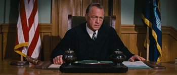Movie still from “Peyton Place” (1957), directed by Mark Robson – A man sitting in a chair in front of a table; Medium shot, Low angle