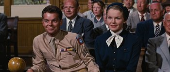 Movie still from “Peyton Place” (1957), directed by Mark Robson – A man and a woman sitting next to each other in front of other people; Medium shot, Low angle