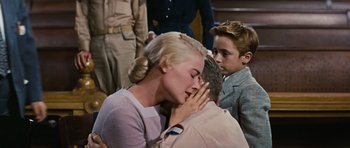 Movie still from “Peyton Place” (1957), directed by Mark Robson – A man and a woman kissing in front of a group of people; Medium shot, High angle