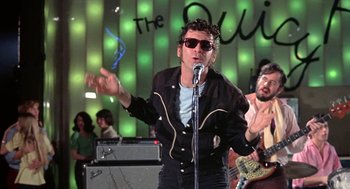 Movie still from “Phantom of the Paradise” (1974), directed by Brian De Palma – A man in a black jacket is singing into a microphone; Medium shot, Low angle