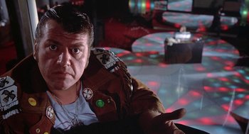 Movie still from “Phantom of the Paradise” (1974), directed by Brian De Palma – A man in a brown jacket sitting in a room with lights; Close Up shot, Low angle