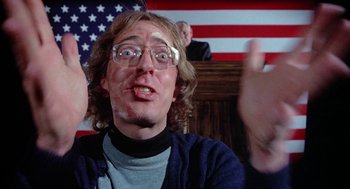 Movie still from “Phantom of the Paradise” (1974), directed by Brian De Palma – A man with glasses is in front of the american flag; Close Up shot, Low angle