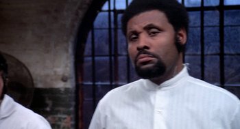 Movie still from “Phantom of the Paradise” (1974), directed by Brian De Palma – A man in a white shirt is standing in front of a brick wall; Close Up shot, Low angle