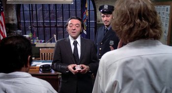 Movie still from “Phantom of the Paradise” (1974), directed by Brian De Palma – A man in a suit and tie talking to two other men in uniform; Medium shot, Over the shoulder angle