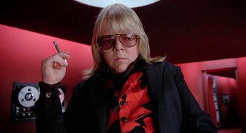Movie still from “Phantom of the Paradise” (1974), directed by Brian De Palma – A woman in a black and red jacket smoking a cigarette; Close Up shot, Low angle