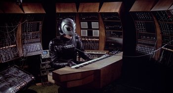 Movie still from “Phantom of the Paradise” (1974), directed by Brian De Palma – A person wearing a helmet and playing a keyboard; Medium shot, High angle
