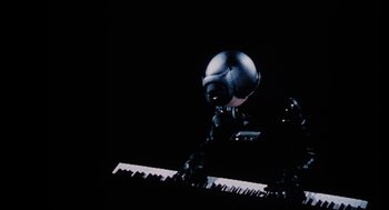 Movie still from “Phantom of the Paradise” (1974), directed by Brian De Palma – A person wearing a helmet playing the piano; Medium shot, Low angle