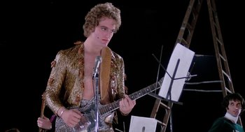 Movie still from “Phantom of the Paradise” (1974), directed by Brian De Palma – A man holding a guitar in front of a microphone; Medium shot, Low angle