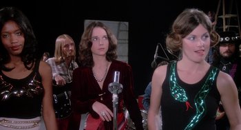 Movie still from “Phantom of the Paradise” (1974), directed by Brian De Palma – A group of women standing next to each other in front of a microphone; Medium shot, Low angle