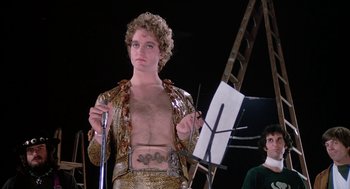 Movie still from “Phantom of the Paradise” (1974), directed by Brian De Palma – A man in a gold outfit holding a painting; Medium shot, Low angle