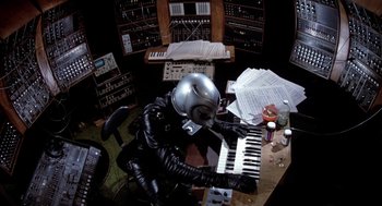 Movie still from “Phantom of the Paradise” (1974), directed by Brian De Palma – A person in a space suit playing a keyboard; Medium shot, High angle