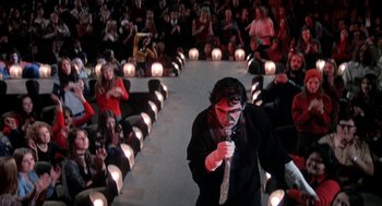 Movie still from “Phantom of the Paradise” (1974), directed by Brian De Palma – A man with a knife in his mouth is walking down the runway; Wide shot, High angle