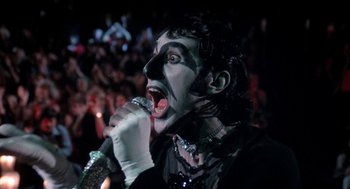 Movie still from “Phantom of the Paradise” (1974), directed by Brian De Palma – A man with a face paint and a microphone in front of an audience; Close Up shot, Low angle