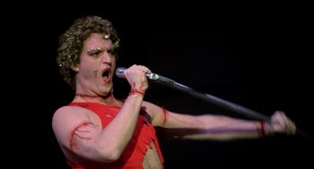 Movie still from “Phantom of the Paradise” (1974), directed by Brian De Palma – A man in red shirt holding a baseball bat; Medium shot, Low angle