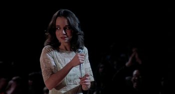 Movie still from “Phantom of the Paradise” (1974), directed by Brian De Palma – A woman in a white dress holding a microphone; Medium shot, Over the shoulder angle