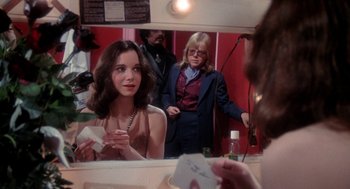 Movie still from “Phantom of the Paradise” (1974), directed by Brian De Palma – A young woman is looking in the mirror while another woman stands in front of a mirror; Medium shot, Over the shoulder angle