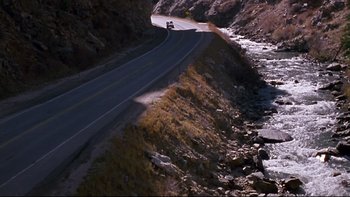 Movie still from “Phantoms” (1998), directed by Joe Chappelle – A truck driving down the side of a mountain road; Extreme Wide shot, High angle