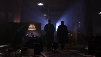 Movie still from “Phantoms” (1998), directed by Joe Chappelle – Two men are standing in a dark room with a lamp on; Wide shot, Low angle