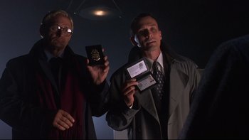 Movie still from “Phantoms” (1998), directed by Joe Chappelle – A man in a suit and tie holding a passport and id; Medium shot, Low angle