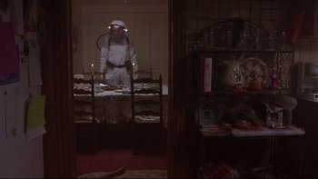 Movie still from “Phantoms” (1998), directed by Joe Chappelle – A man in a spacesuit standing next to a table with food; Wide shot, Low angle