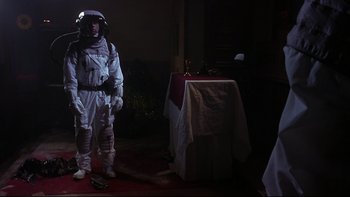 Movie still from “Phantoms” (1998), directed by Joe Chappelle – A man in a spacesuit standing in front of a table; Wide shot, Low angle