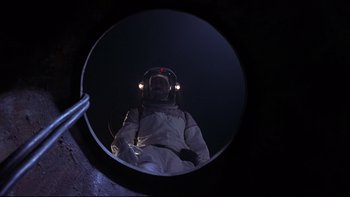 Movie still from “Phantoms” (1998), directed by Joe Chappelle – A person in a spacesuit is reflected in a mirror; Medium shot, Overhead angle